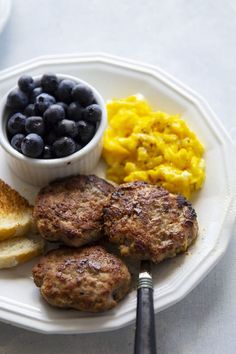 a white plate topped with meat patties and blueberries next to toasted bread