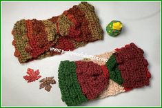 two crocheted hats with bows and leaves on the top one is red, green, yellow and brown