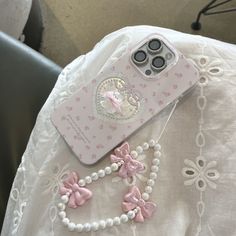 an iphone case with pink bows and pearls on the cover, sitting on top of a white lace tablecloth