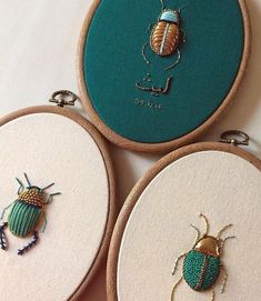 three embroidery hoop frames with embroidered bugs on them, one in green and the other in gold