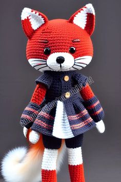 a crocheted stuffed fox wearing a coat and skirt with fur tail is standing on a gray surface