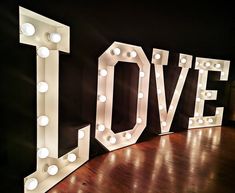 the word love spelled out with light bulbs in front of a black wall and wooden floor