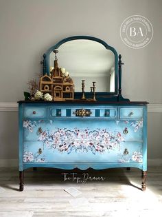 a blue dresser with flowers painted on it and an ornate mirror above the top drawer