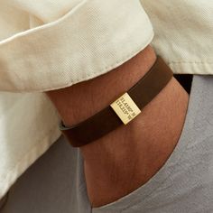 a person wearing a brown leather bracelet with a gold plated name tag on it