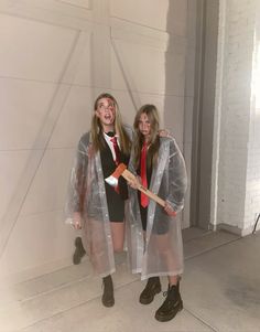 two girls dressed in plastic raincoats and rubber boots, one holding a shovel