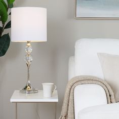 a table with a lamp on it next to a white chair and a potted plant