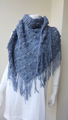 a white mannequin wearing a blue crocheted shawl with fringes