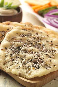 two flat breads topped with seeds and seasoning on a cutting board next to vegetables