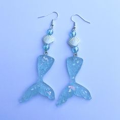 a pair of blue glass mermaid earrings with seashells and pearls hanging from them