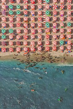 an aerial view of the beach with umbrellas and people swimming in the ocean water