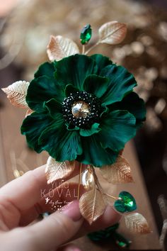 a hand holding a green flower on top of a piece of paper with leaves and jewels