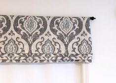 a window curtain with an ornate pattern hanging on the side of a white wall next to a clock