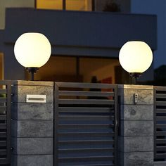 two lamps sitting on top of a cement wall next to a gate with a building in the background