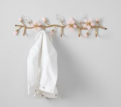 a white shirt hanging on a wall next to a coat rack with pink flowers and leaves