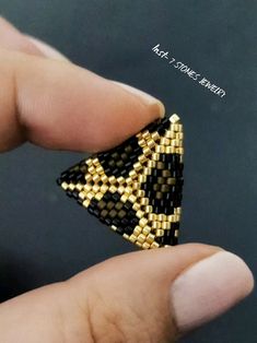 a hand holding a small black and gold beaded triangle brooch on it's finger