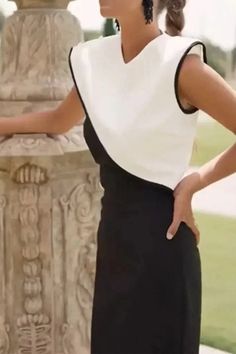 a woman in a black and white dress standing next to a stone pillar with her hands on her hips