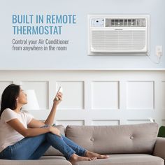 a woman is sitting on the couch and looking up at an air conditioner that reads built in remote thermostat control your air conditioner from anywhere in the room