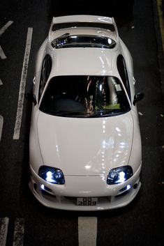 a white sports car parked on the side of the road at night with its lights on