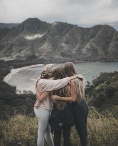 three women hugging each other on top of a hill