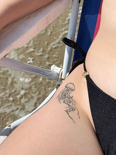 a woman with a tattoo on her stomach sitting in a chair next to the water