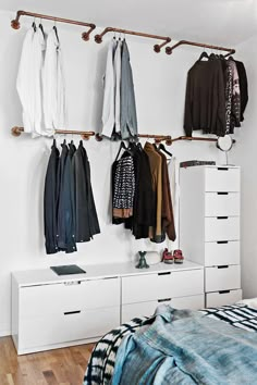 an organized bedroom with clothes hanging on the wall