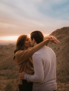 a man and woman kissing in the desert at sunset with their arms around each other