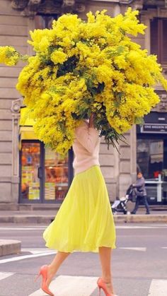 a woman walking across a street carrying a bunch of yellow flowers