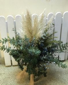 a vase filled with lots of flowers on top of a floor next to a white fence