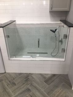 a bathroom with white tiles and gray flooring, shower head and handset on the wall