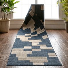 a blue and beige area rug on the floor in front of a window with potted plants