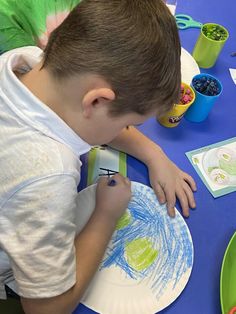 a young boy is painting on a paper plate