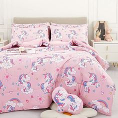 a pink bed with unicorns and stars on the comforter is next to a stuffed animal