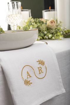 the table is set with white linens and gold embroidered monogrammed napkins