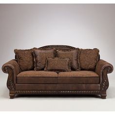 a brown leather couch with pillows on it's arms and back cushions, sitting in front of a gray background