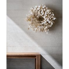 a white wreath hanging on the wall next to a wooden table and chair in front of it