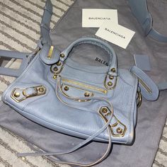 Balenciaga Nano City Bag In Blue (Greyish). Crossbody Bag In A Good Condition, Has White Stain Inside The Bag And Noticed Scratch On The Right Side. Overall Looks Great Comes With A Removable Strap And A Dust Bag. Base Length: 7 In Height: 4.5 In Width: 2.25 In Drop: 2.5 In Drop: 21 In Bags Balenciaga, White Stain, Balenciaga Bag, City Bag, Blue And Gold, Right Side, Gold Hardware, Balenciaga, Crossbody Bag