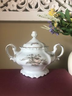 a white tea pot sitting on top of a table next to a vase filled with flowers