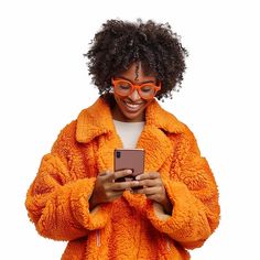 a woman in an orange coat and glasses looking at her cell phone while standing against a white background