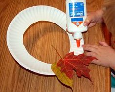 someone is making a paper plate wreath with fall leaves and glue on the front part