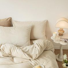 an unmade bed with white sheets and pillows on top of it next to a night stand