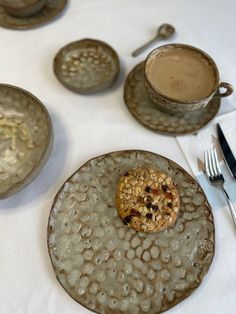 there is a cookie on the plate next to two cups and spoons, along with silverware