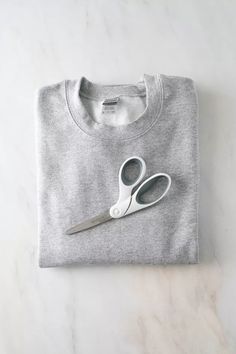 a pair of scissors sitting on top of a gray t - shirt that is cut in half