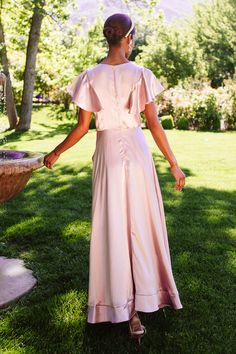 a woman standing in the grass wearing a pink dress