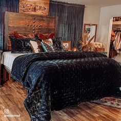 a bed with black bedspread and wooden headboard in a bedroom next to a mirror