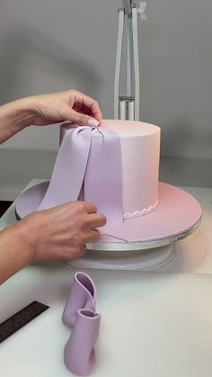 a woman is decorating a pink cake with purple ribbons and bows on the top