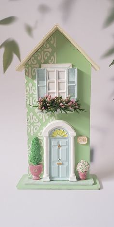 a doll house with green walls and white shutters on the window sill next to potted plants