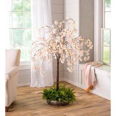 a white tree with pink flowers in a living room next to a chair and window