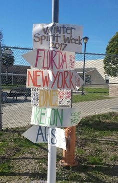 a pole with signs on it in front of a chain link fence and street light