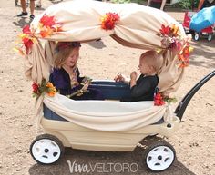 two small children in a wagon with flowers on the top and canopy over them, outside