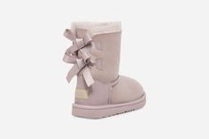 We added sweet silky bows to your little one's favorite boot, but kept the super-soft sheepskin feel they love. Built to move the way kids do, each boot features a rocker-bottom shape for a barefoot feel and our ultra-lightweight outsole for traction and durability. Pair with the same style in our women's sizes for cute mini-me moments.The outsole of this product is either a sugarcane EVA outsole, which is a responsible compound using sugarcane foam that allows us to reduce dependency on fossil fuels by replacing petroleum-based ethylene, or a Treadlite by UGG® outsole.This product was made in a factory that supports women in our supply chain with the help of HERproject. This collaborative initiative creates partnerships with brands like ours to empower and educate women in the workplace. Ugg Boots With Bows, Ugg Store, Mini Baileys, Bailey Bow, Kids Uggs, Favorite Boots, Classic Boots, Slipper Shoes, Slipper Boots